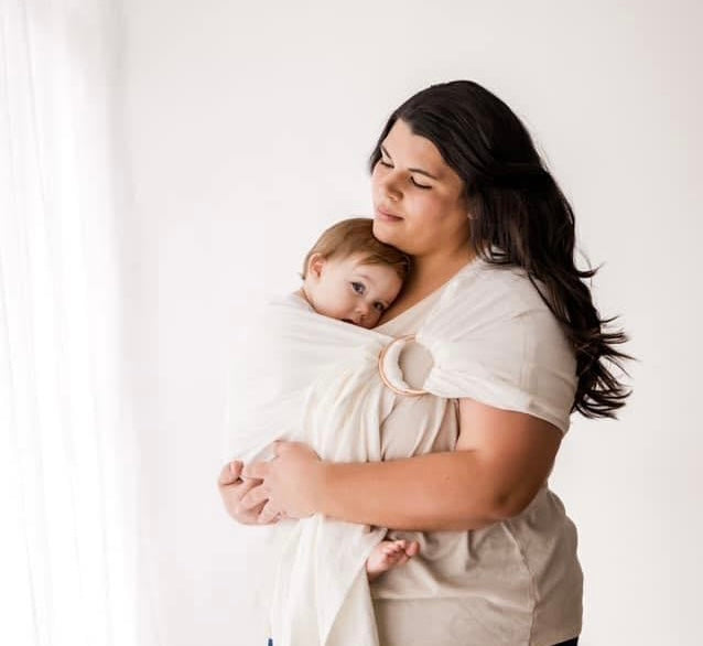 Mother kissing baby in brown ring sling baby carrier