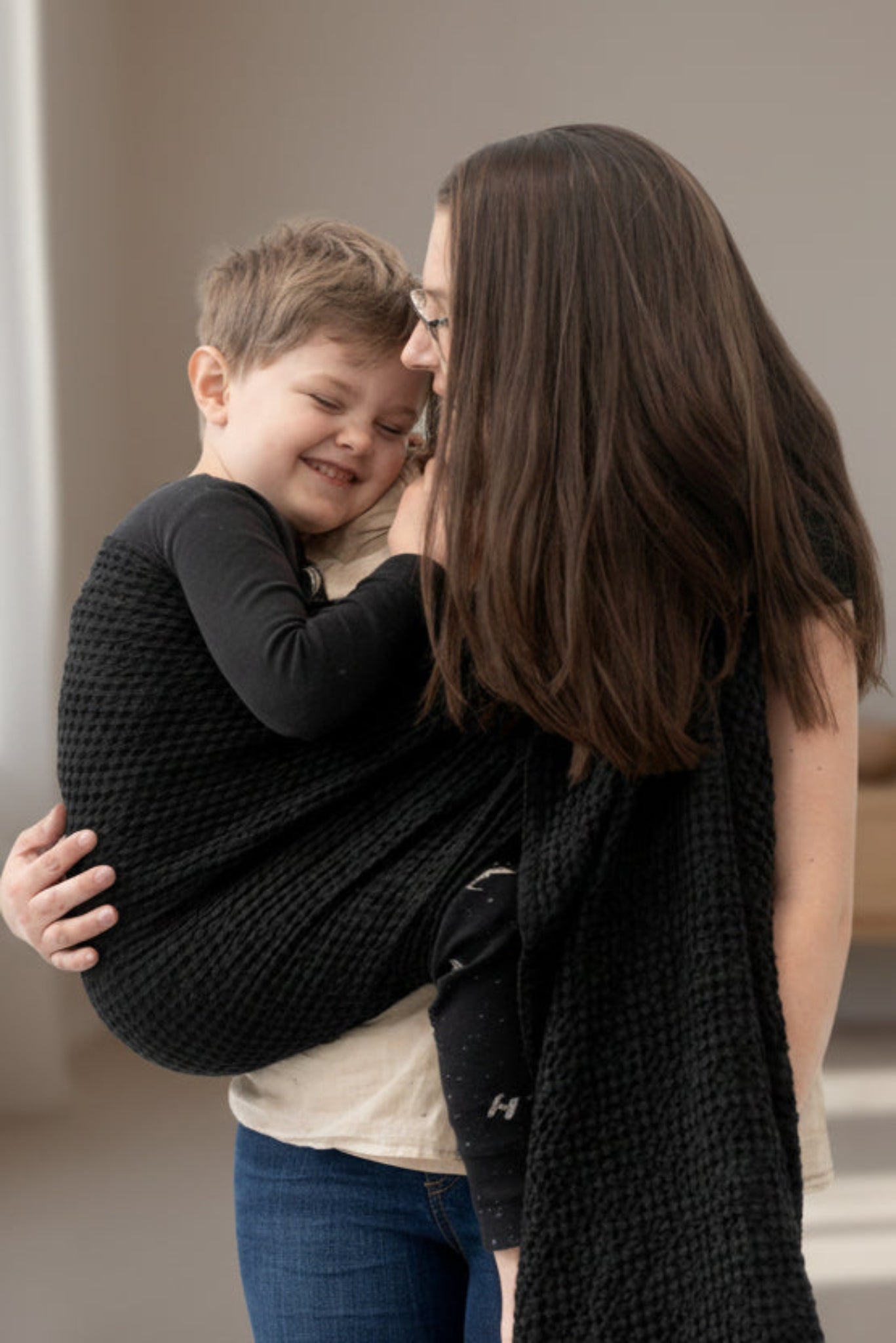 Woman holding a child in a black woven wrap against a white background