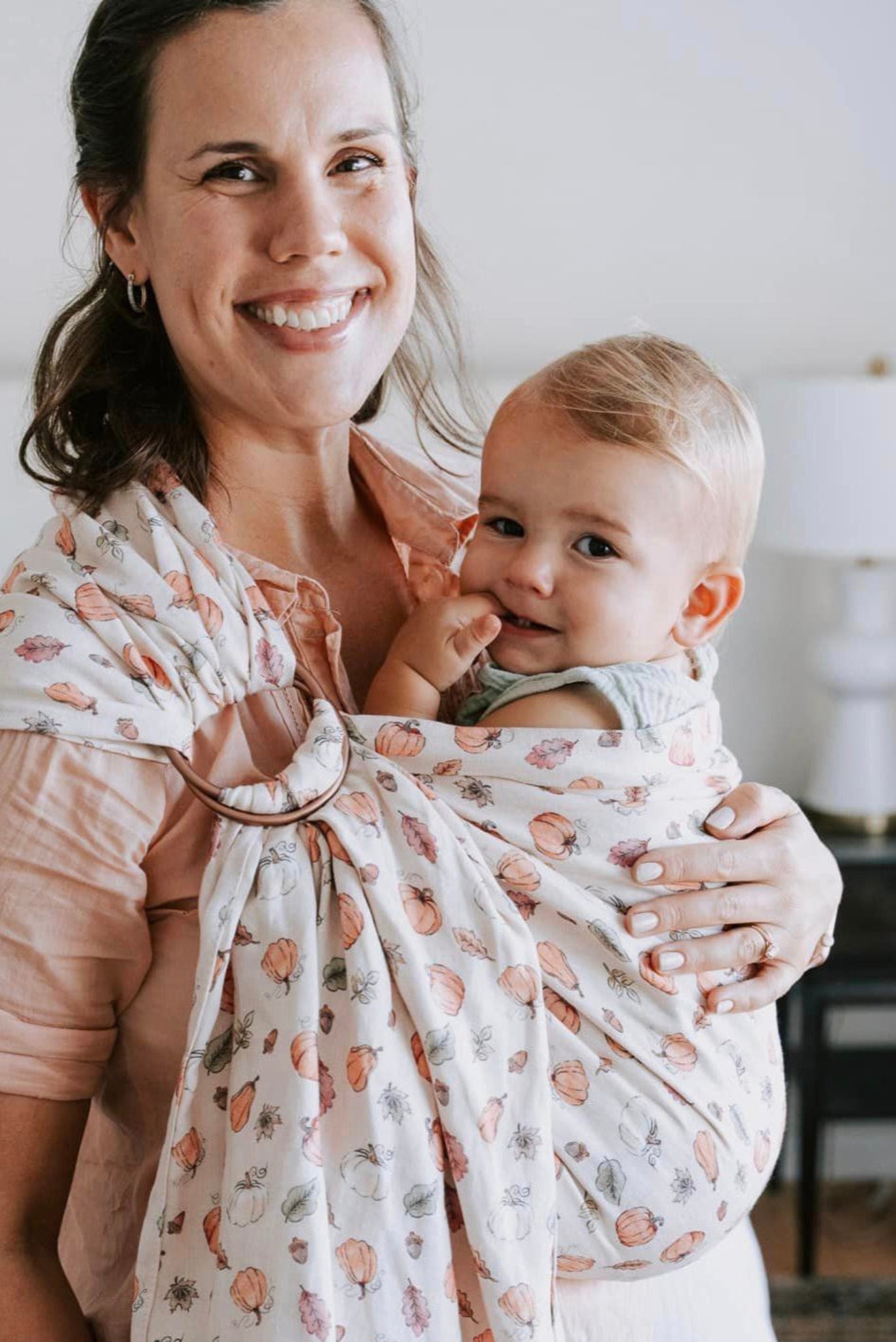 Woman holding a baby wrapped in a floral ring sling baby carrier in a home setting