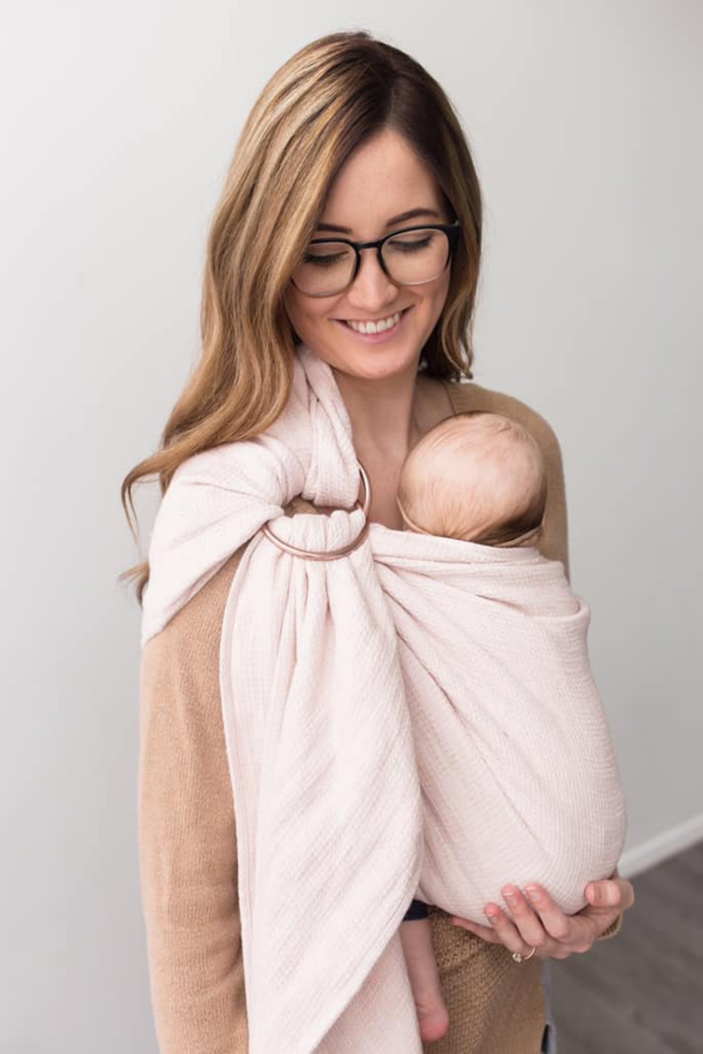 Woman holding a baby wrapped in a pink ring sling against a white background