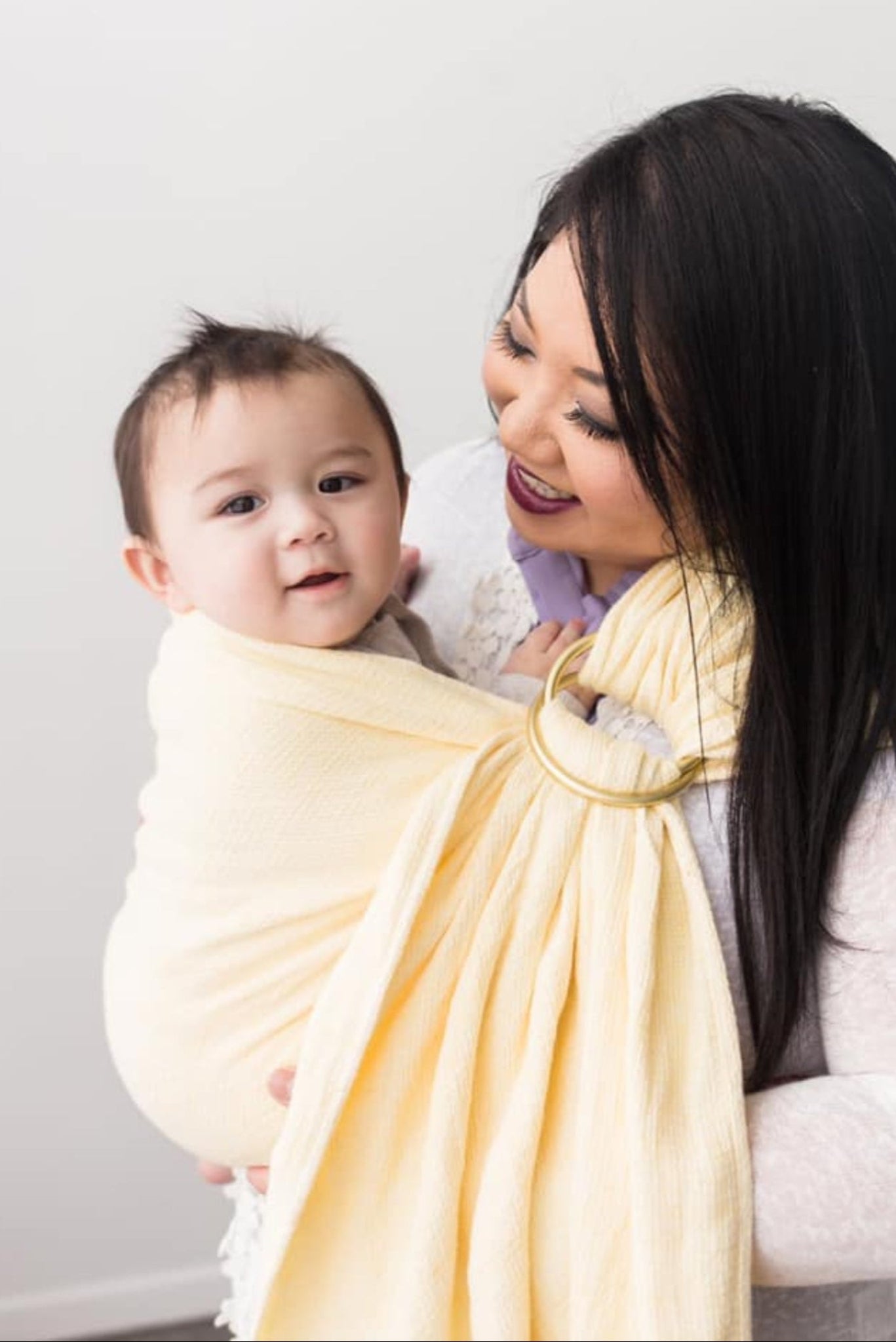 Woman holding a baby wrapped in a yellow sling against a white background
