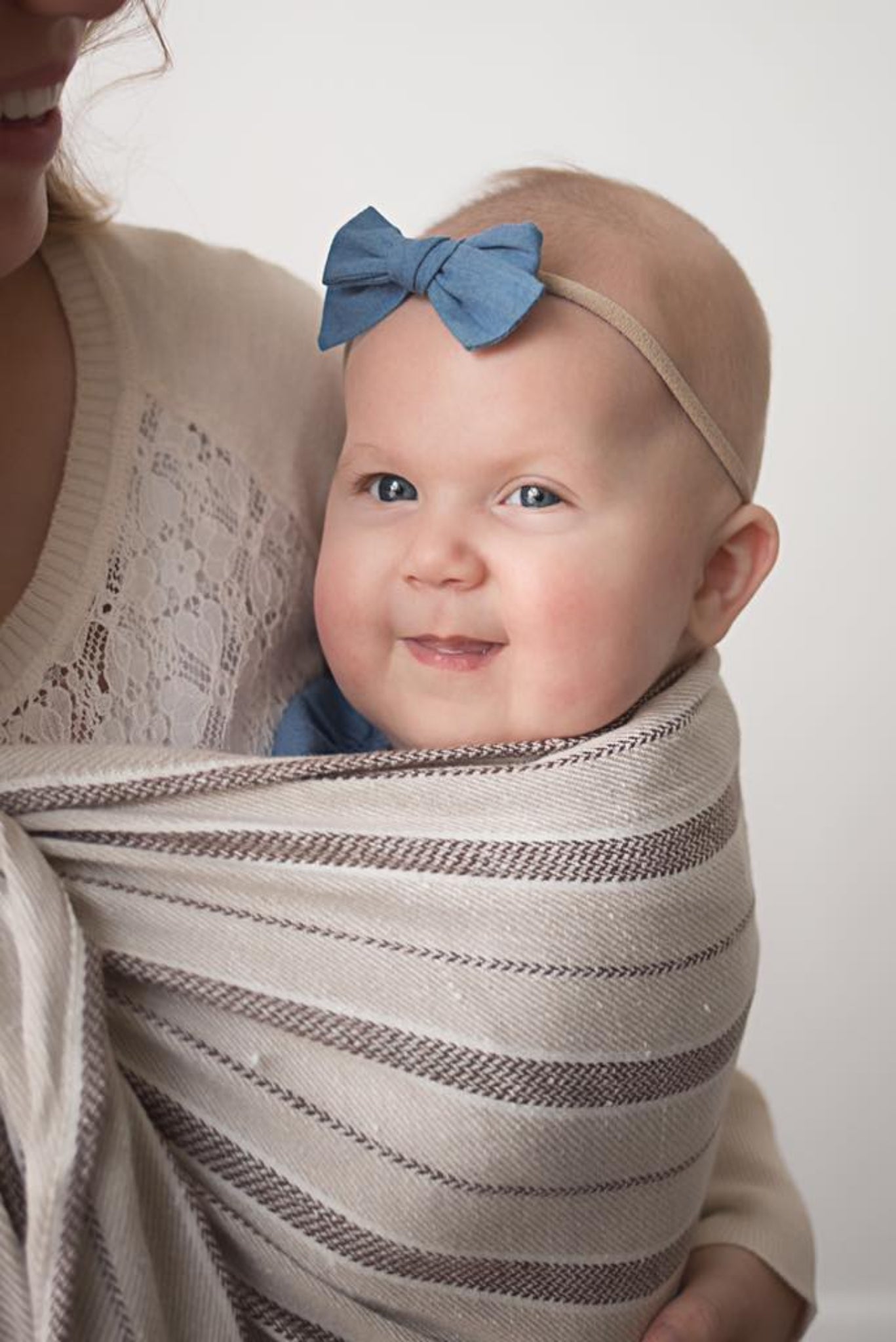 Baby wrapped in a striped blanket with a blue bow headband, smiling.