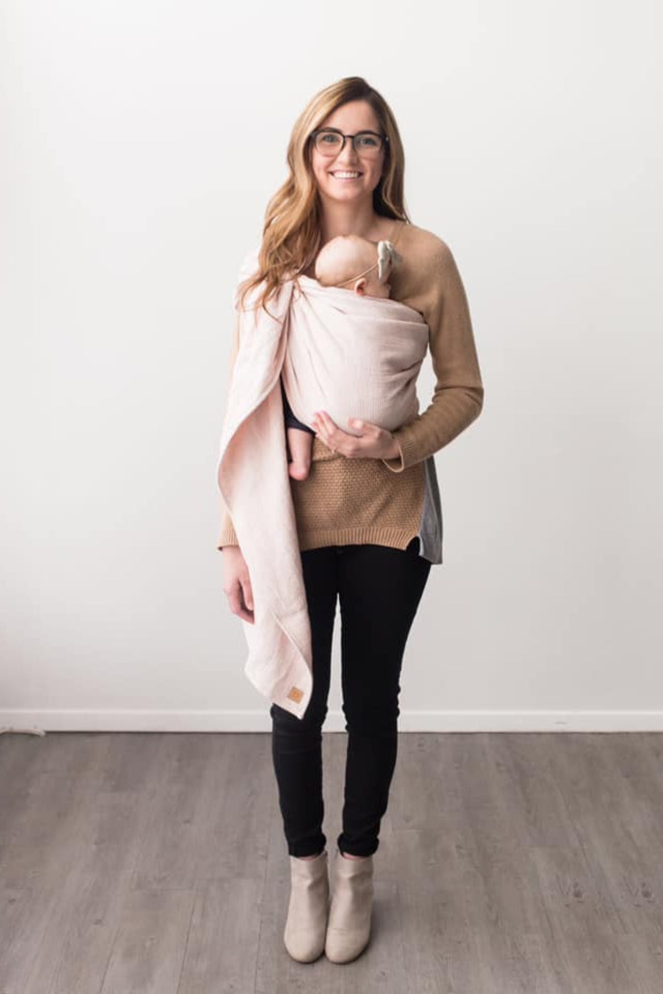 Woman holding a baby in a sling against a white wall