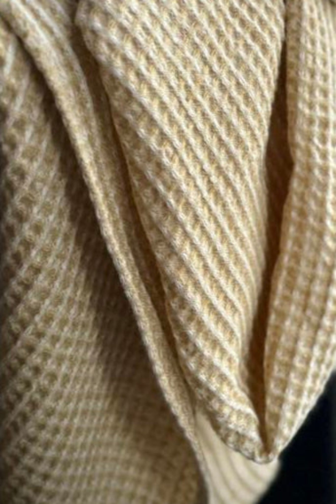 Close-up of a muted mustard waffle-weave fabric with a textured soft folds.