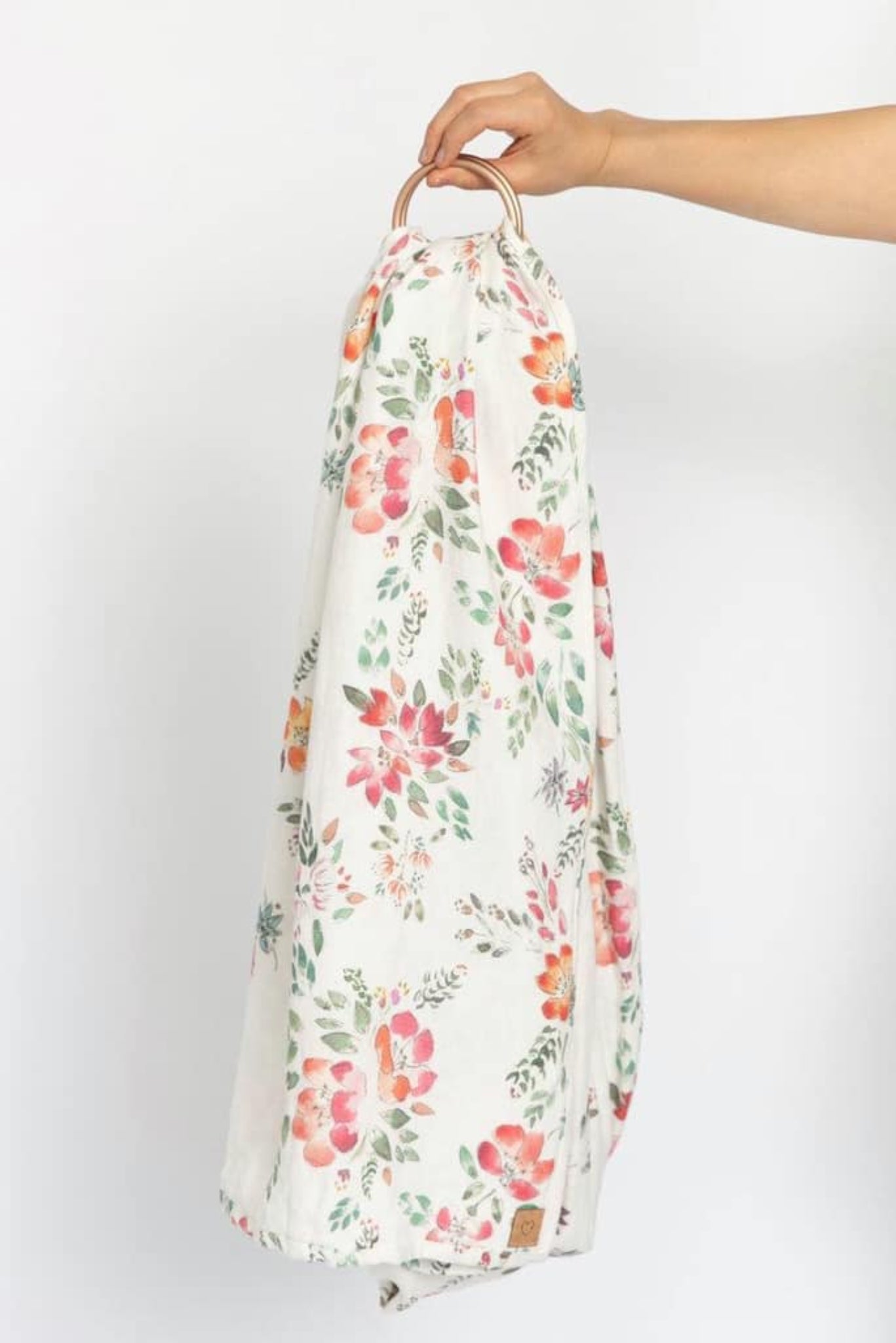 Floral-patterned baby ring sling baby carrier held by a hand against a white background
