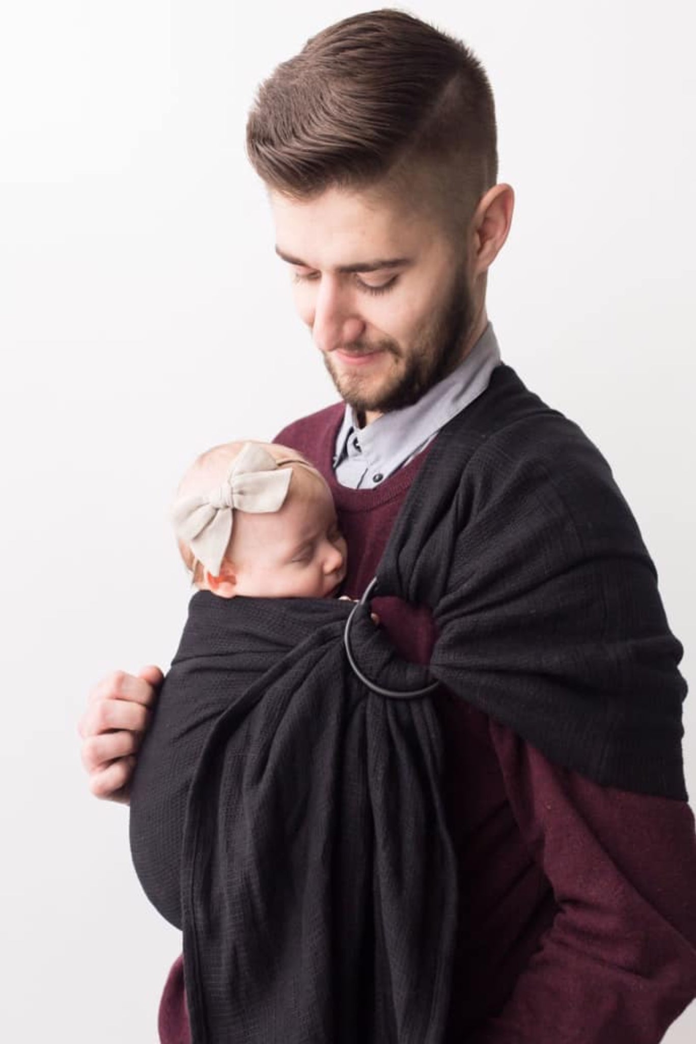 Man holding a baby in a sling against a white background