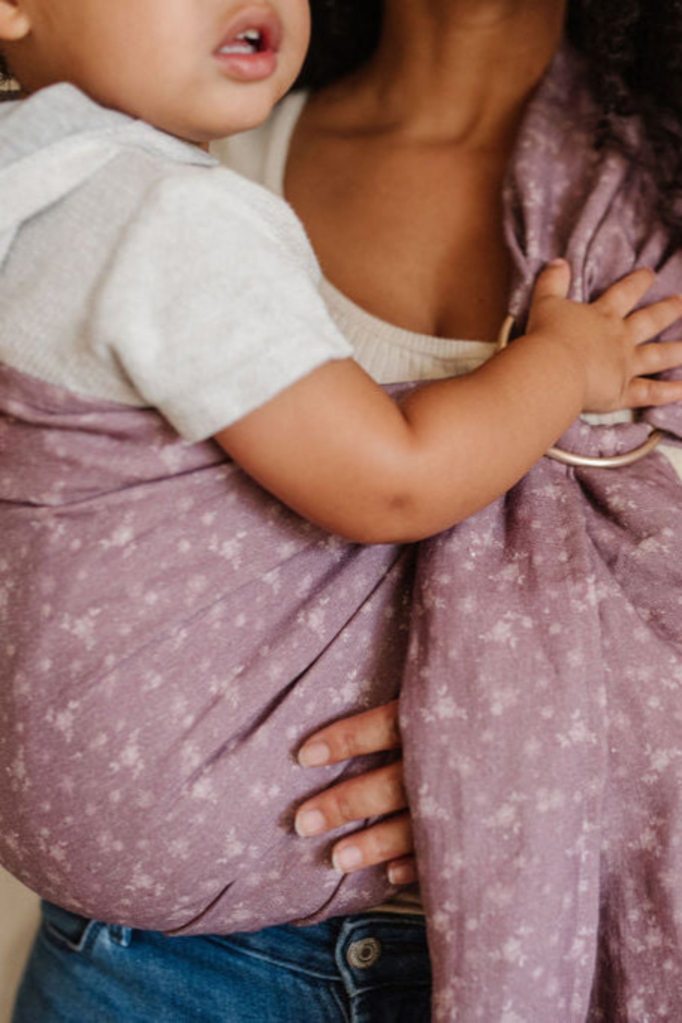Person holding a child wrapped in a vintage designed mauve floral ring sling baby carrier.