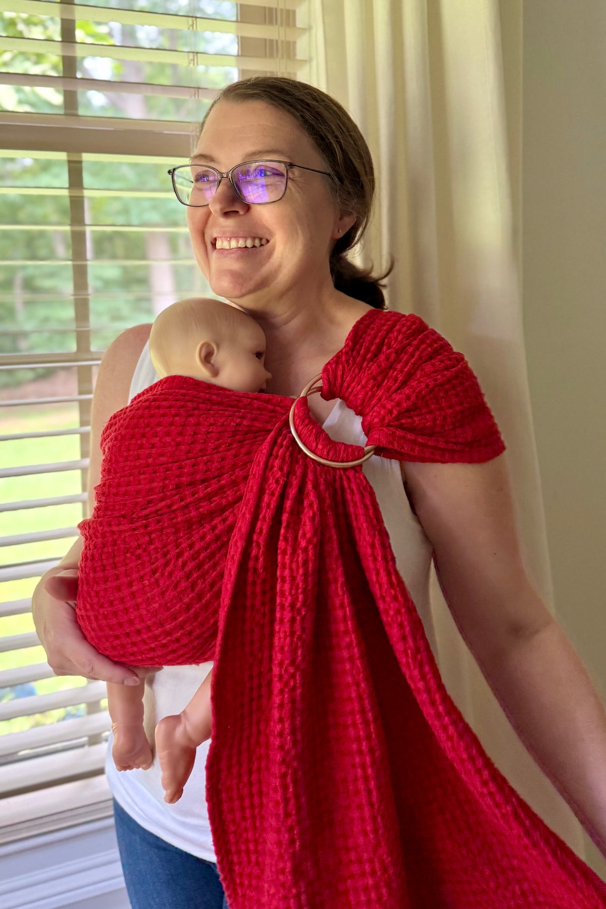 Woman holding a baby in a red sling against a window background