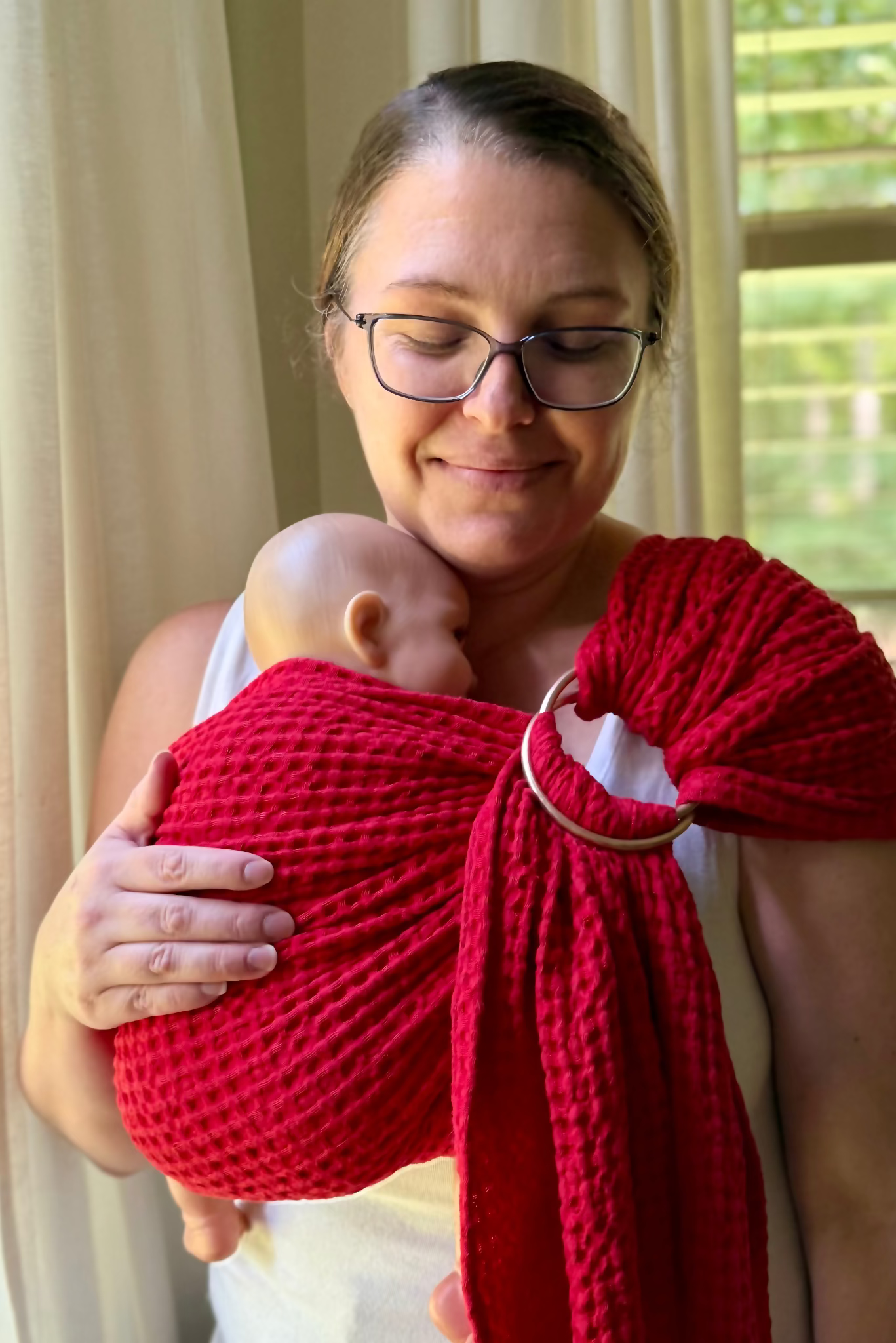 Woman holding a baby in a red sling against a neutral background