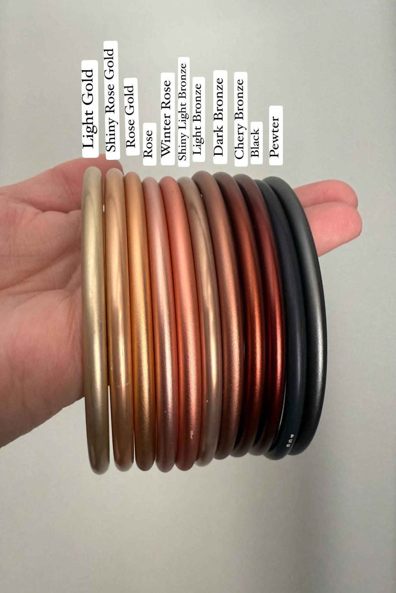 Stack of metal ring sling rings in various colors held by a hand on a neutral background
