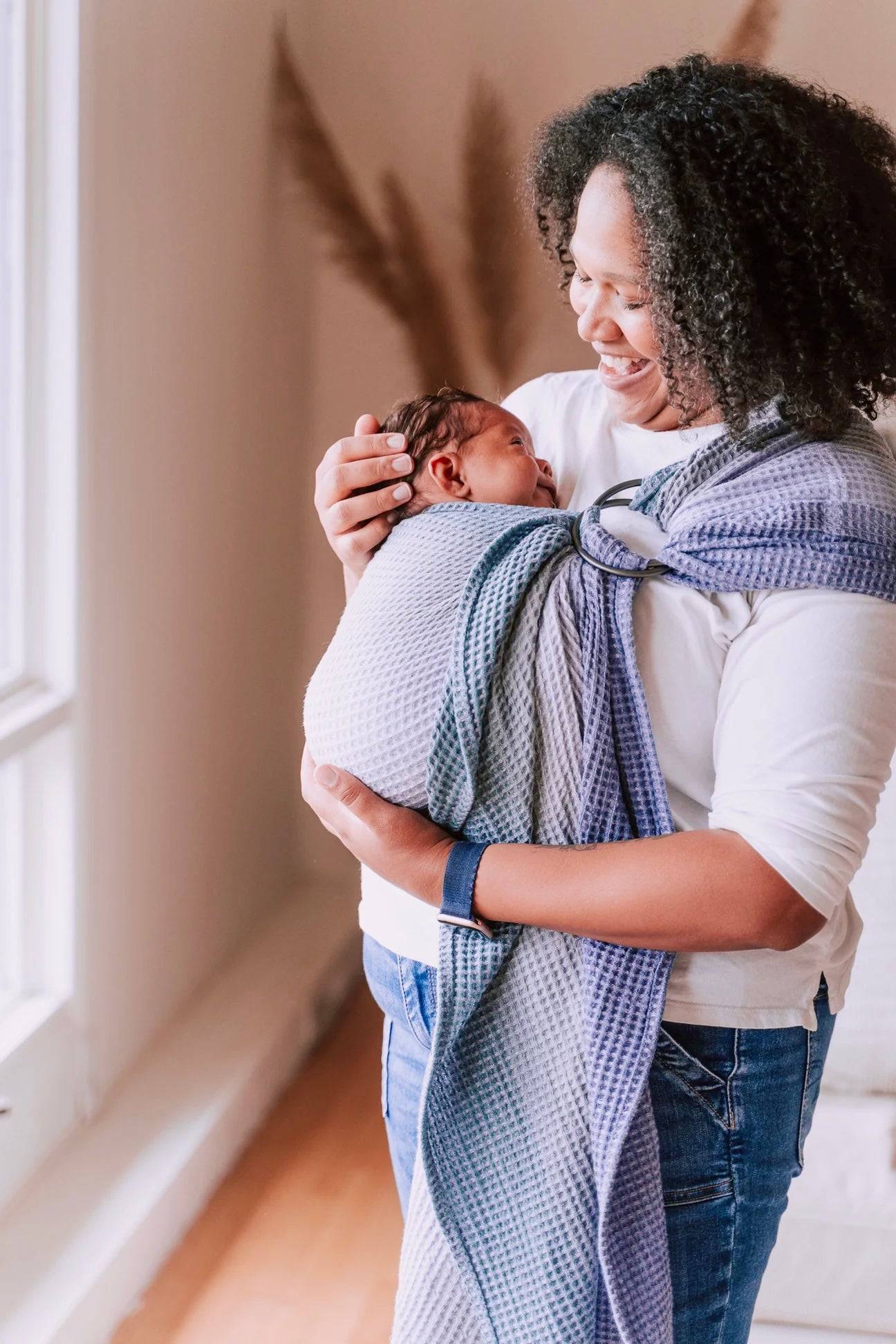 A person is holding a sleeping baby wrapped in a blue and white striped ring sling carrier.