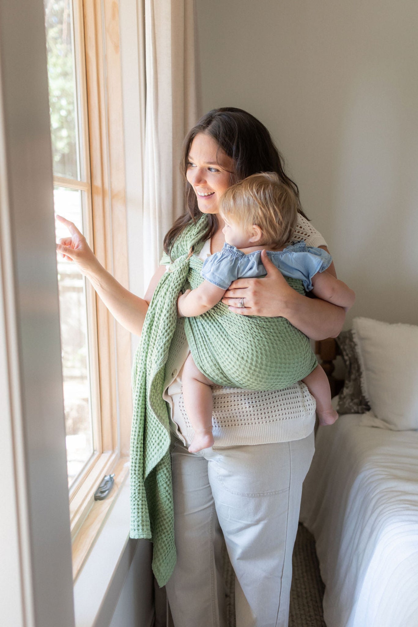 Woman holding a baby in a ring sling baby carrier by a window in a home setting
