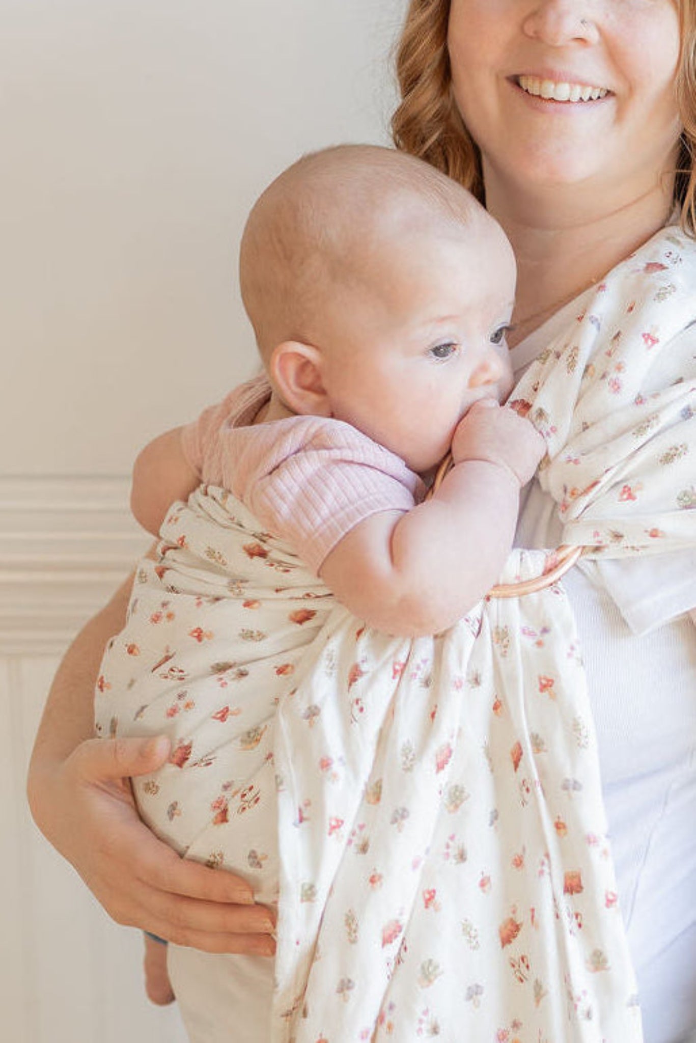 Woman holding a baby wrapped in a floral wrap against a white wall.