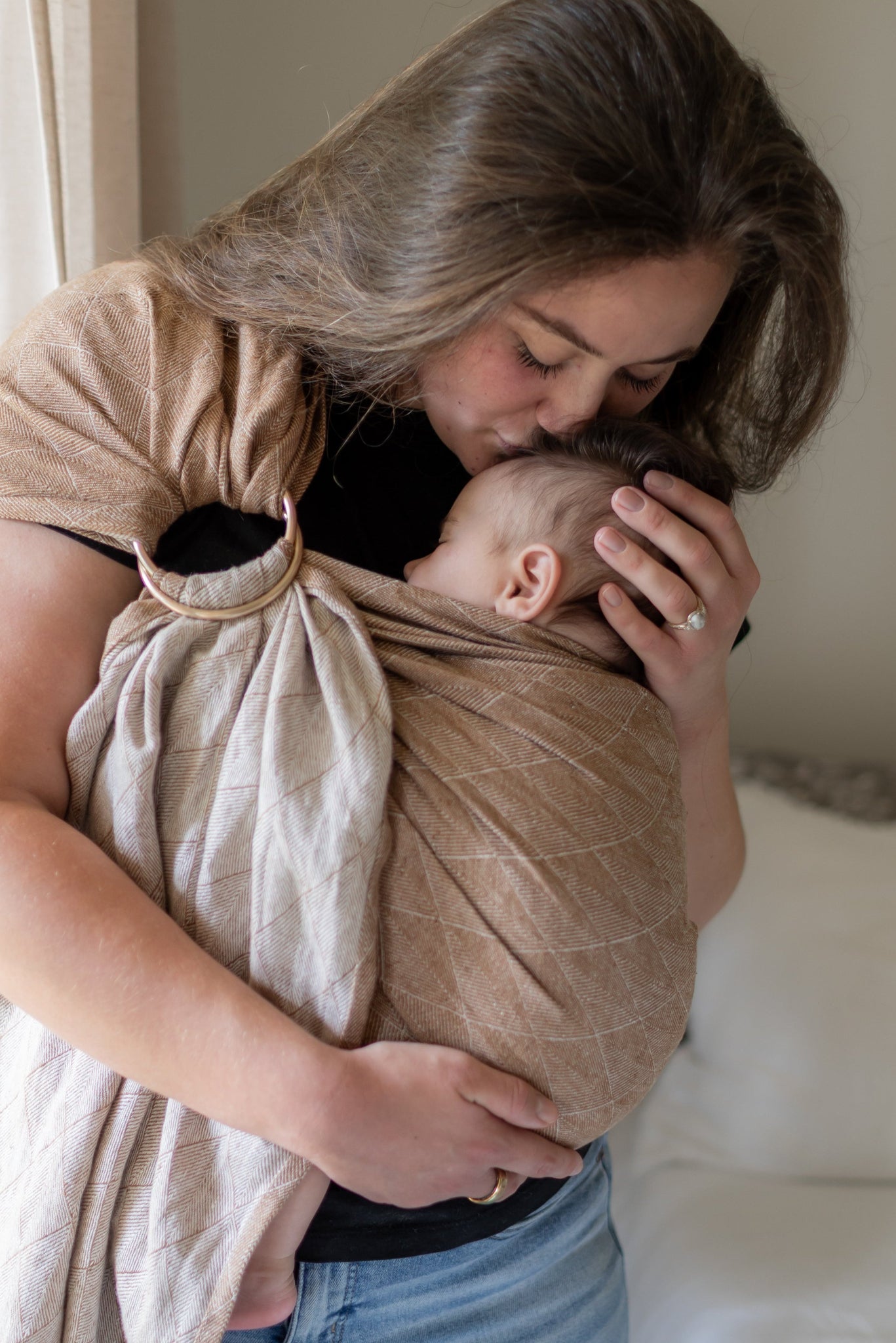 Woman holding a baby in a beige wrap against a neutral background