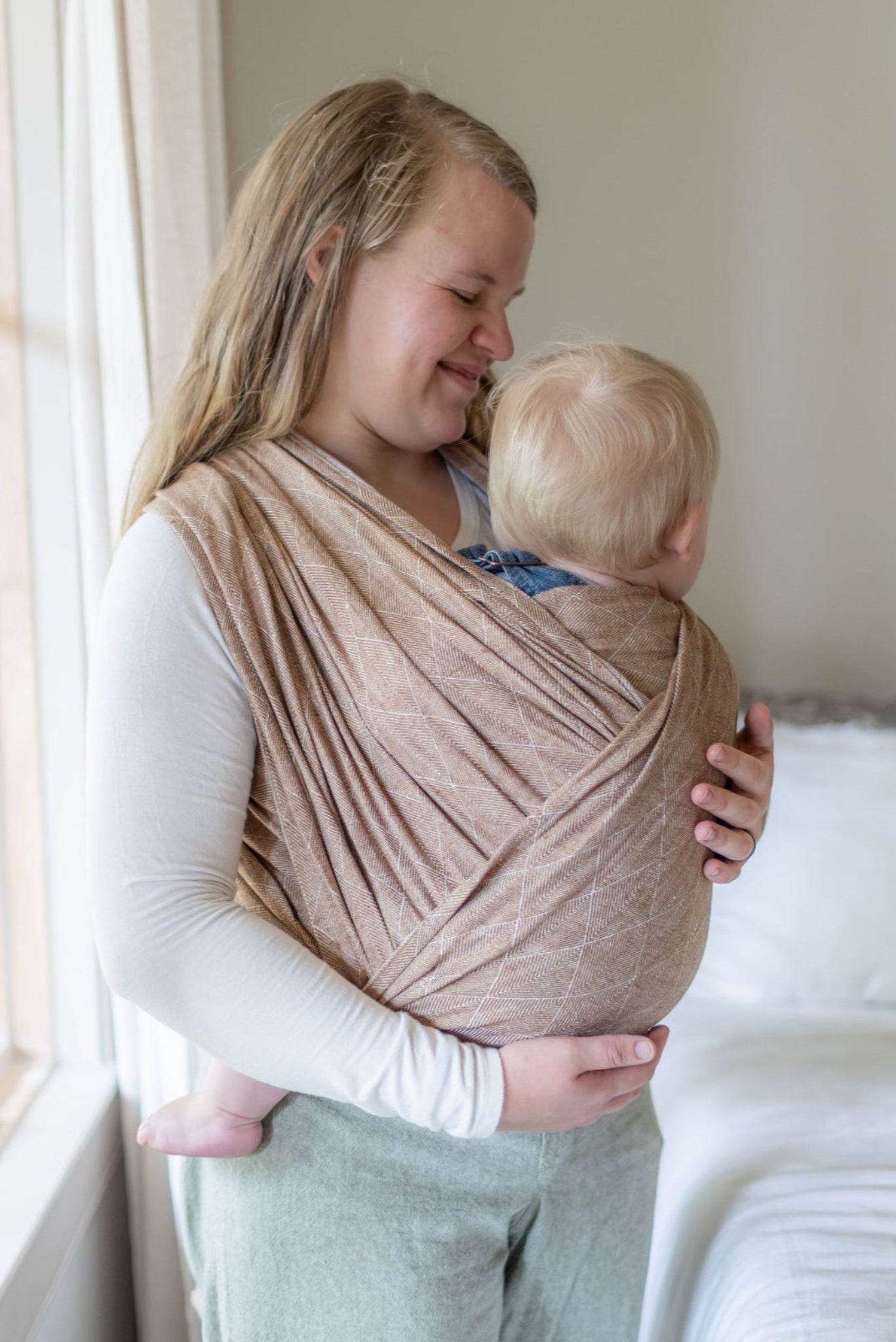 Woman holding a baby in a sling by a window
