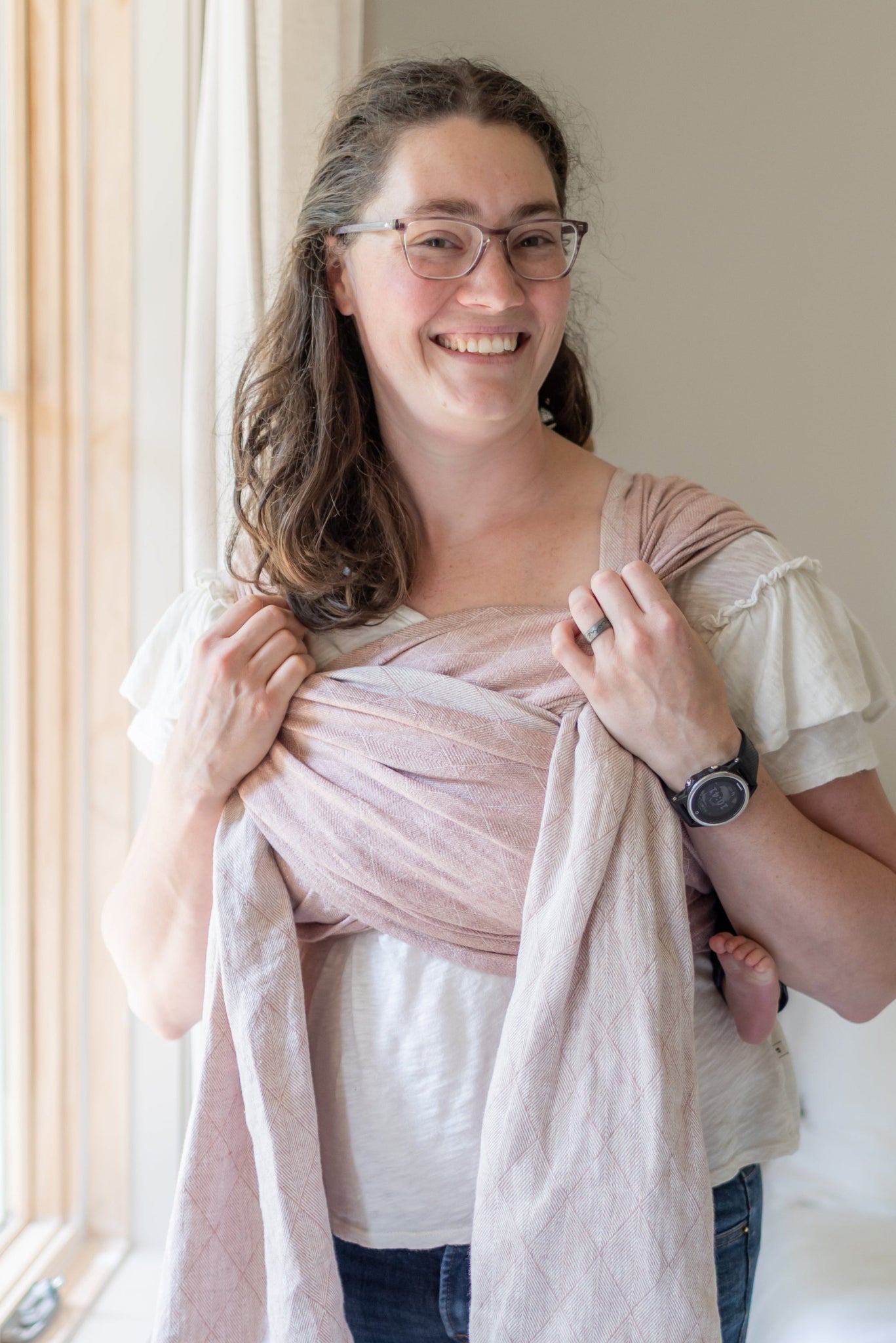 Woman holding a baby wrapped in a pink blanket by a window