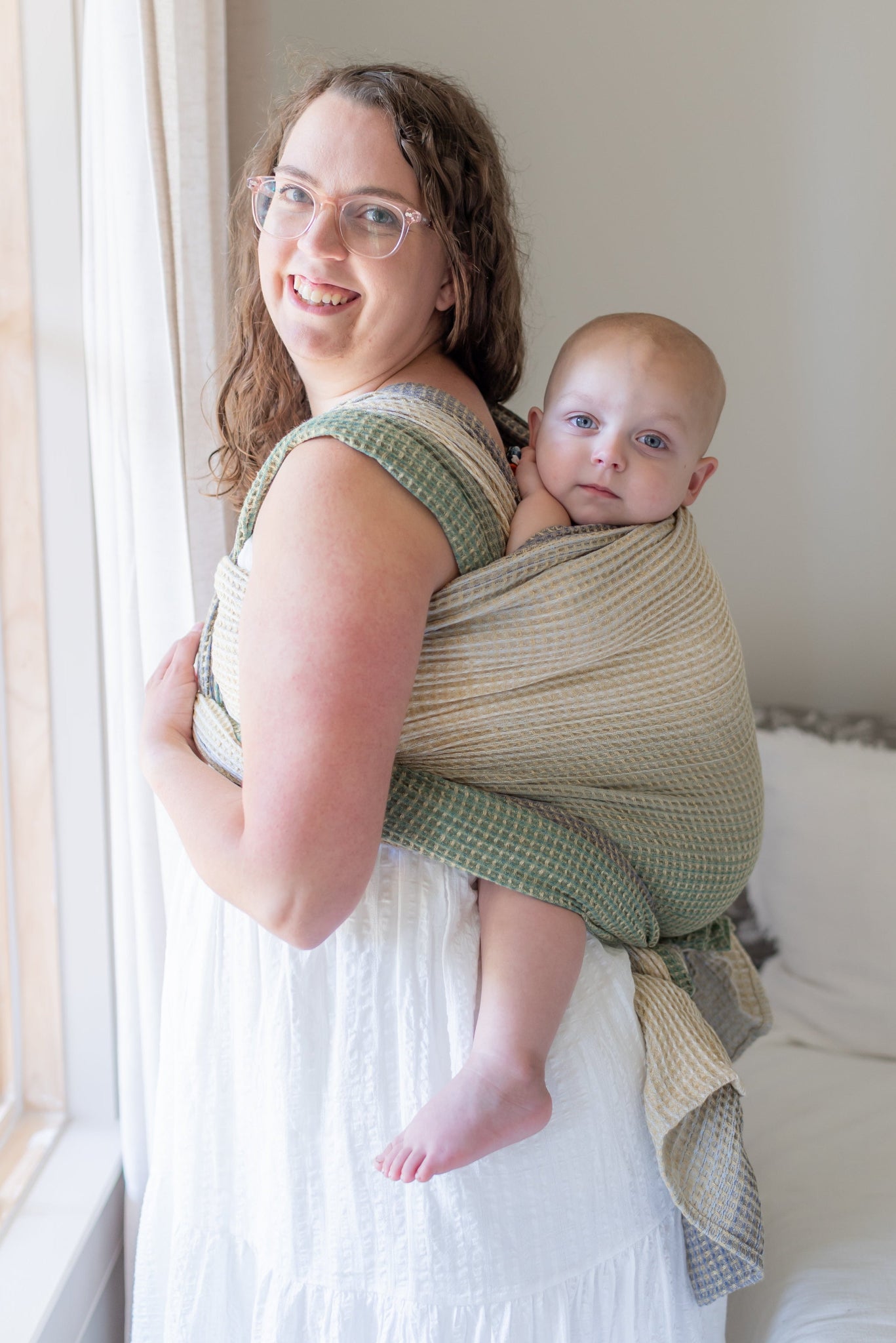 Woman holding a baby in a sling by a window