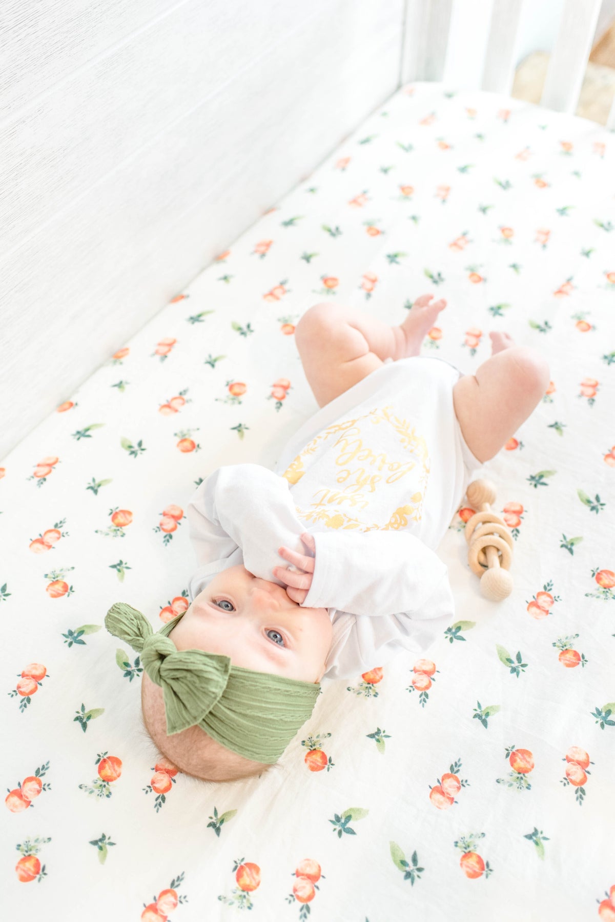 Infant laying a white linen crib sheet with peach details